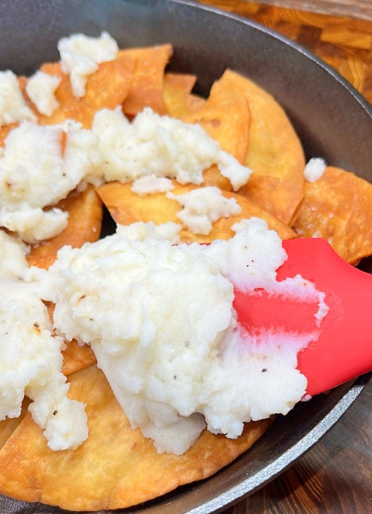 A skillet with crispy tortilla chips topped with melted cheese. A red spatula is lifting the cheese.