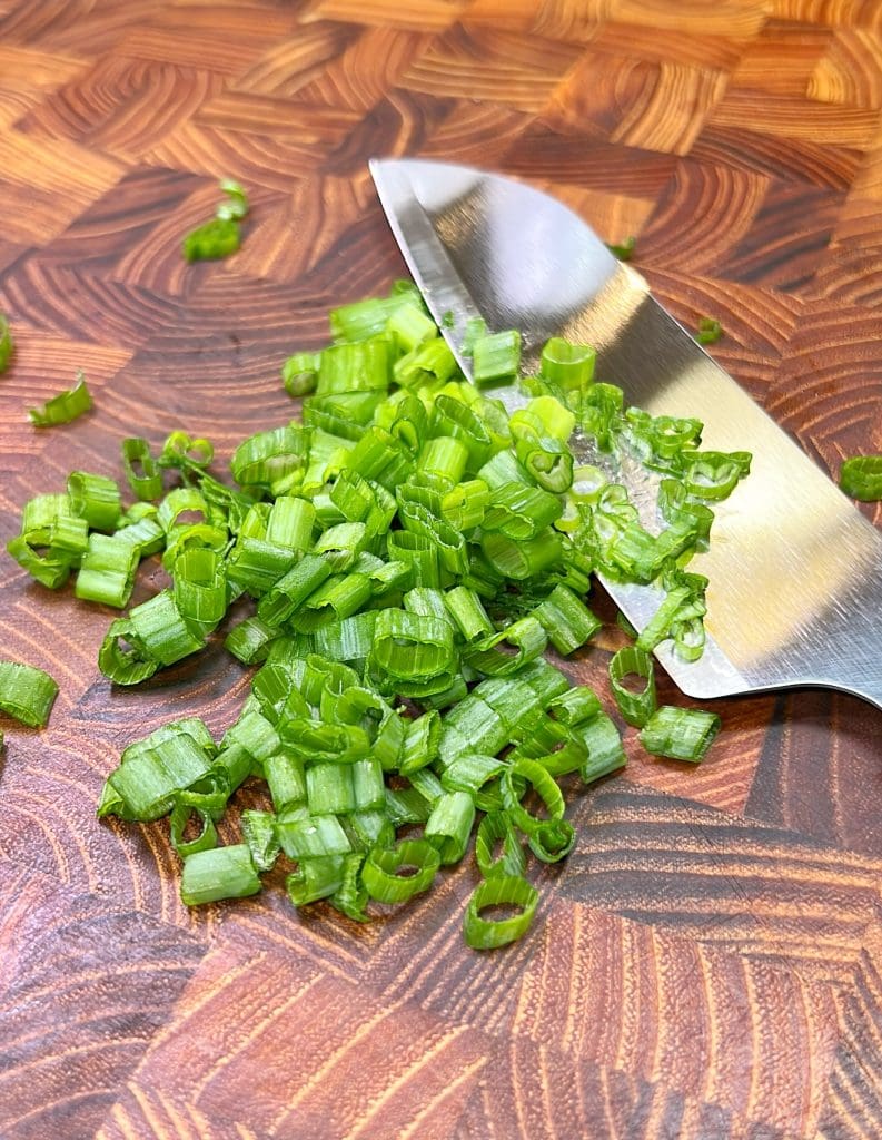 Chopped green onions with a knife on a wooden cutting board.