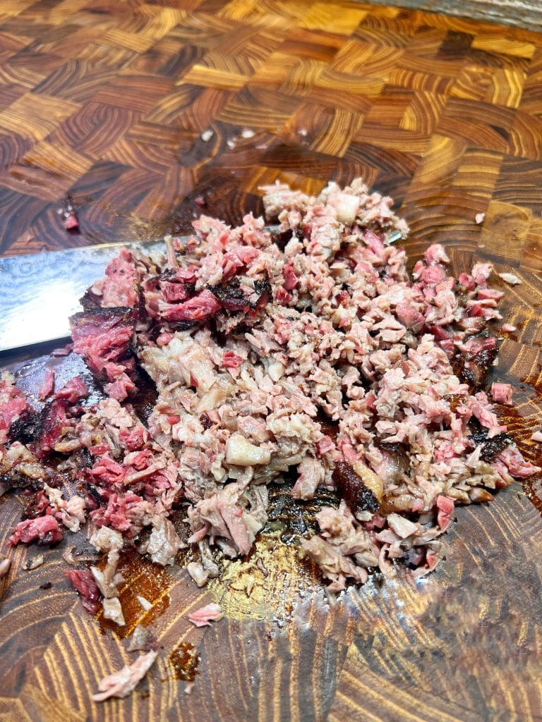 Chopped pieces of cooked meat on a wooden cutting board next to a knife.