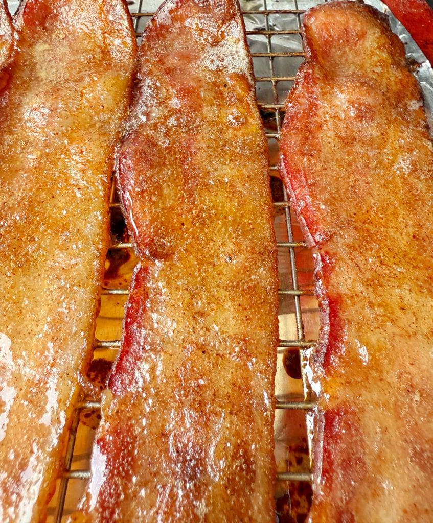 Close-up of several strips of caramelized bacon on a wire rack. The bacon glistens with a coating of brown sugar, giving it a glossy and crispy appearance.