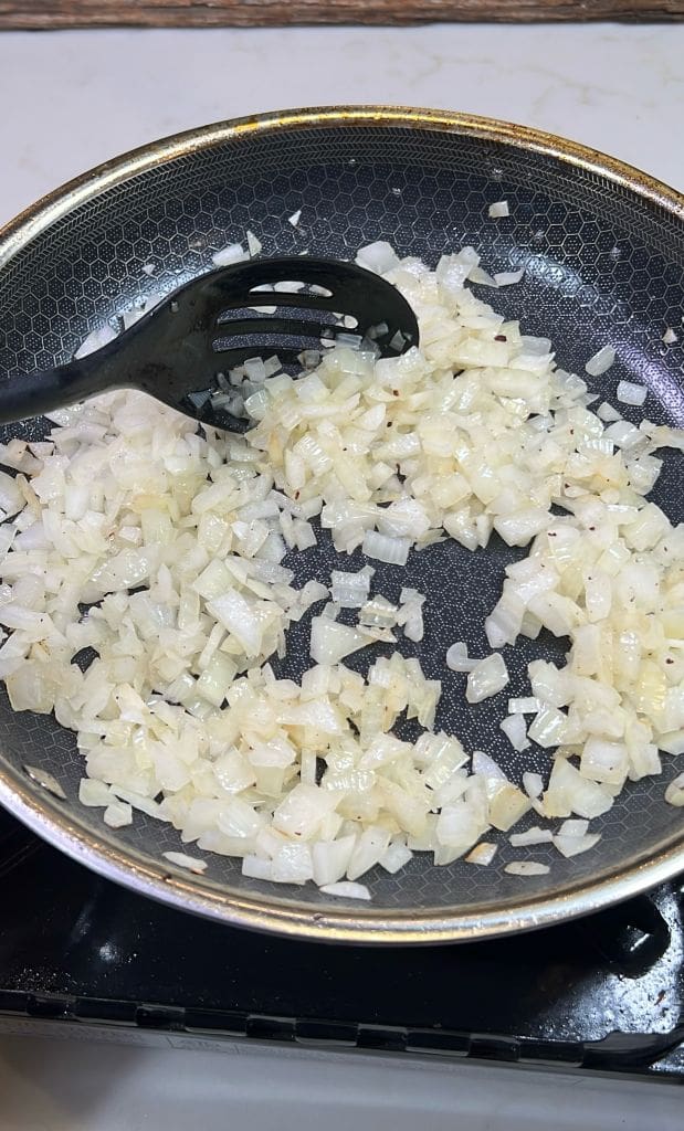 Chopped onions being sautéed in a nonstick frying pan with a black spatula.