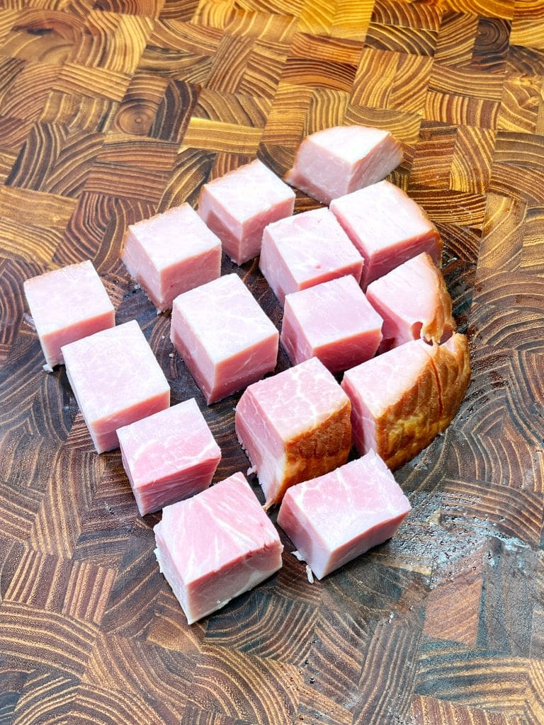 Cubes of raw, pink fish neatly arranged on a wooden chopping board with a distinctive swirling pattern.