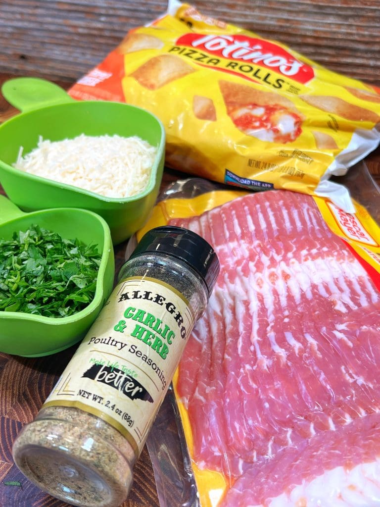 A bag of Totinos Pizza Rolls, a pack of bacon, a bottle of garlic herb seasoning, and small bowls of shredded cheese and chopped herbs are arranged on a wooden surface—perfect ingredients for an irresistible snack recipe: Bacon Wrapped Pizza Rolls.