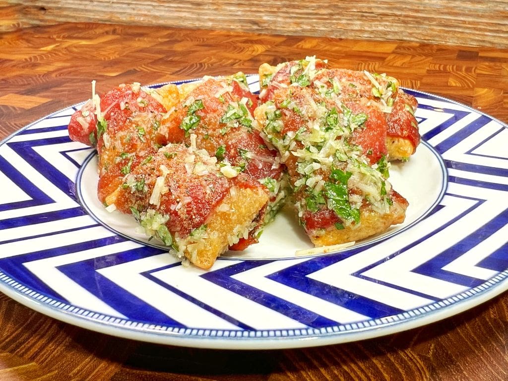 A plate with stuffed tomatoes topped with herbs and cheese. The dish is placed on a blue and white zigzag patterned plate, set against a wooden background.