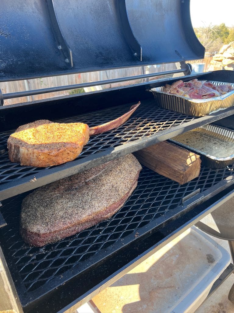 A smoker with a tomahawk steak cooking over indirect heat to prepare for reverse searing.,