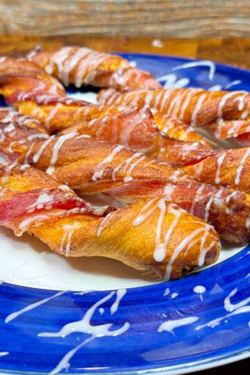Twisted pastry sticks drizzled with icing are arranged on a blue plate with a white center. The wooden background adds a rustic touch to the presentation.