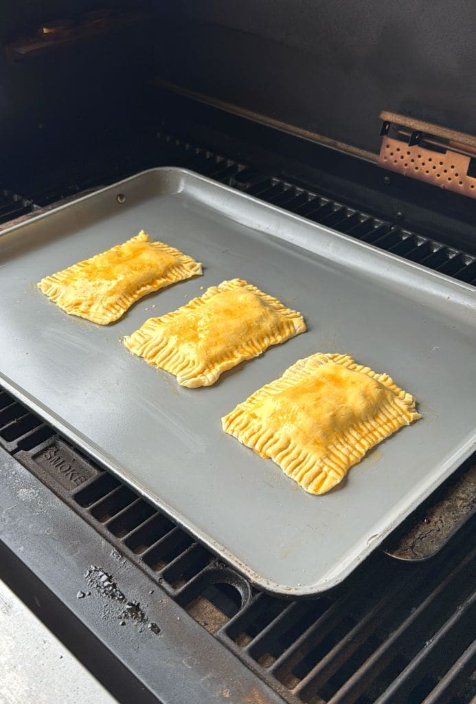 Three rectangular pastries with crimped edges are on a baking tray inside an oven. They appear golden brown and freshly baked.