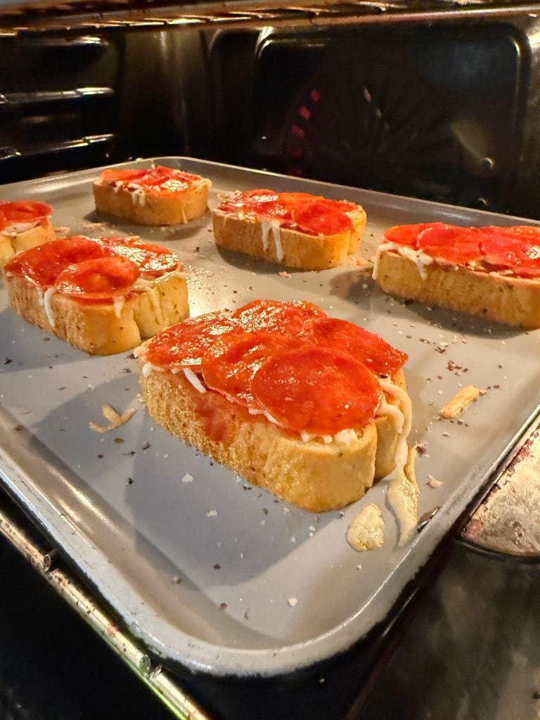 Slices of Texas Toast pizza topped with tomato sauce, cheese, and pepperoni are baking on a tray in the oven.