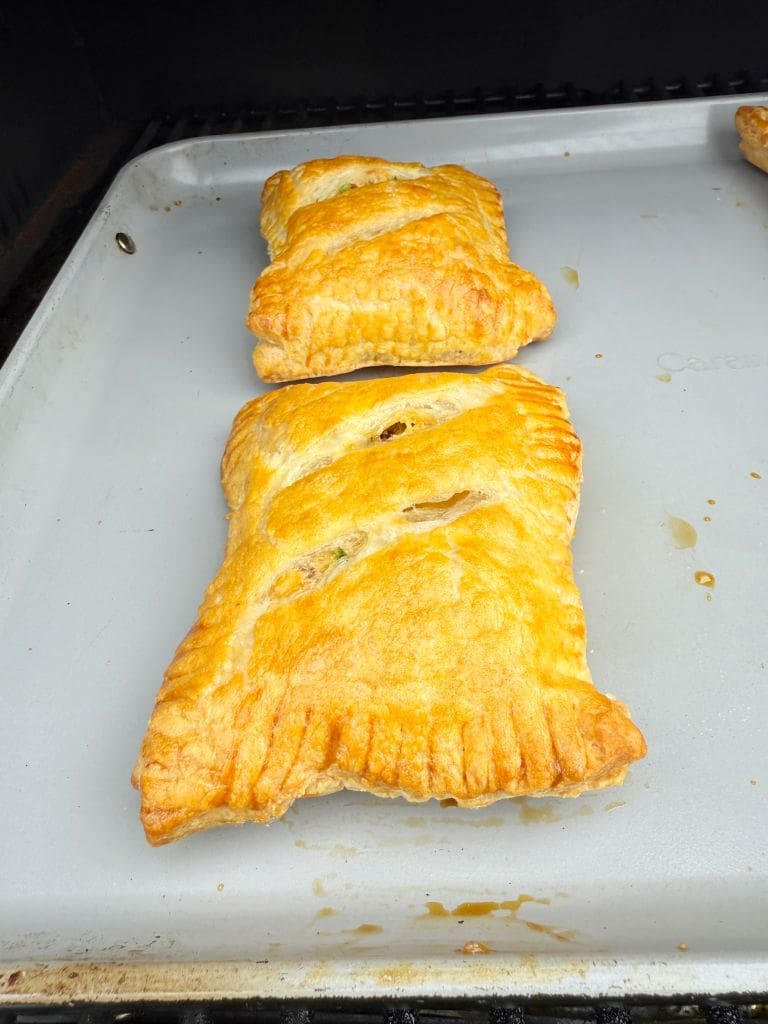Two golden-brown puff pastries with visible flaky texture lie on a baking tray. They are rectangular with crimped edges, suggesting a filled interior.