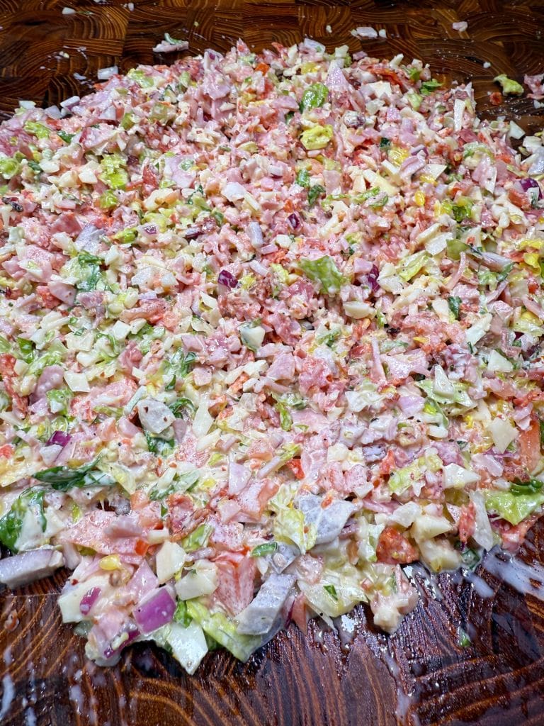 A colorful salad spread across a wooden surface, featuring chopped vegetables including cucumbers, tomatoes, red onions, and lettuce, mixed with a creamy dressing.