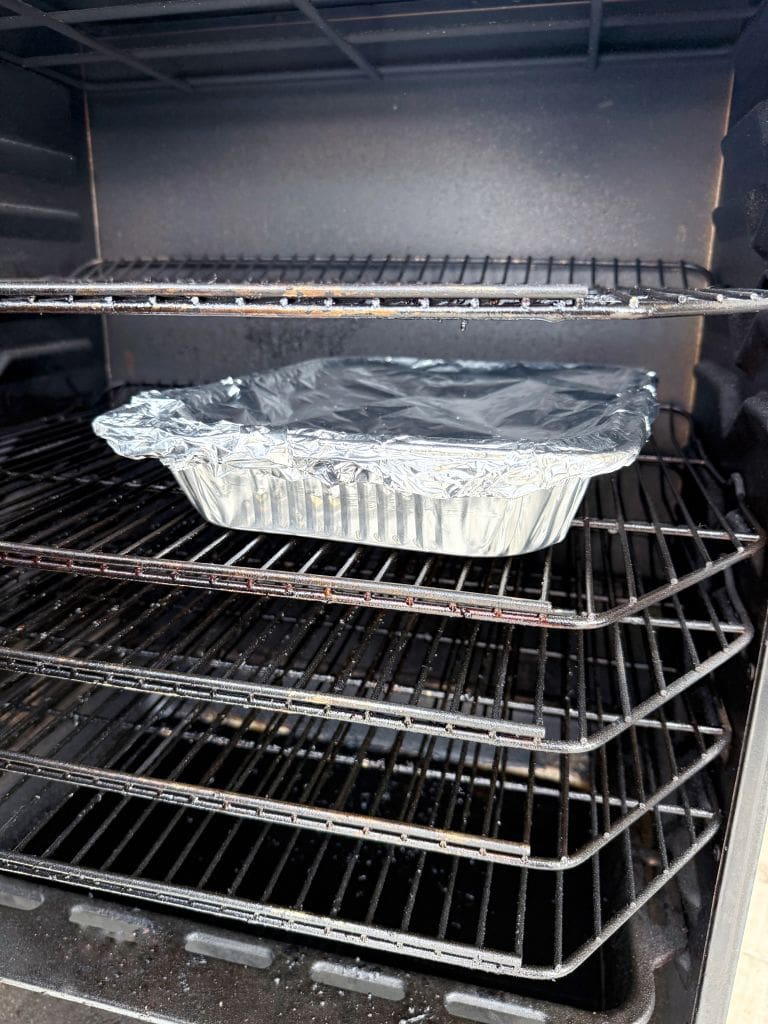 A foil-covered aluminum tray sits on a middle rack inside an open oven, ready for baking. The oven has multiple wire racks and is turned off, appearing clean and unused.