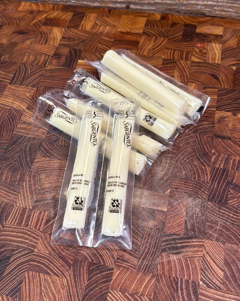 Several individually wrapped Sargento mozzarella string cheese sticks are scattered on a dark, patterned wooden surface.