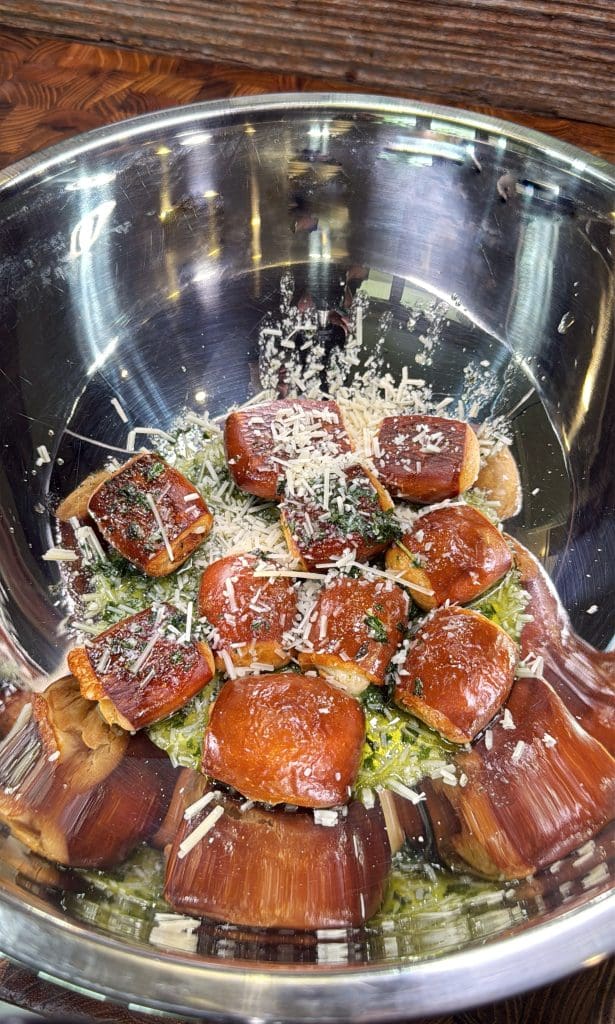 A metal bowl filled with a salad topped with several glazed, breaded bites, garnished with grated cheese and herbs. The bowl sits on a wooden surface.