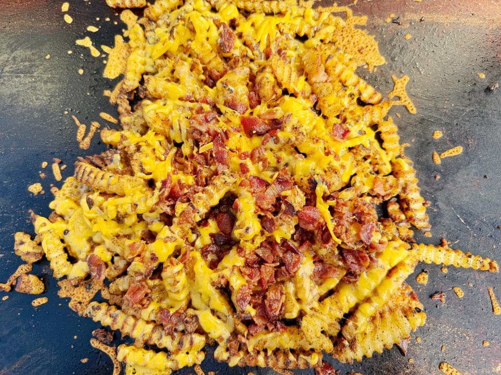 Crinkle-cut French fries topped with melted cheddar cheese and crispy bacon pieces, served on a dark flat surface.
