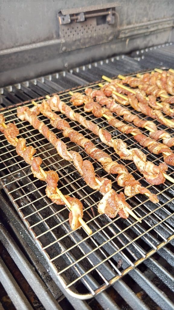 Several skewers of seasoned meat are arranged on wire racks, cooking on a grill inside a barbecue smoker.