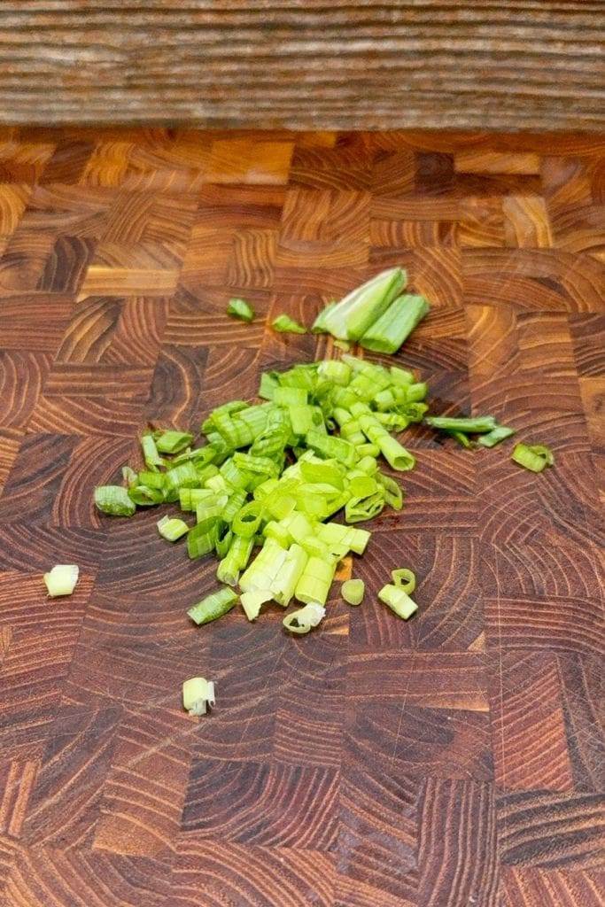 Chopped green onions scattered on a wooden cutting board with a geometric pattern.