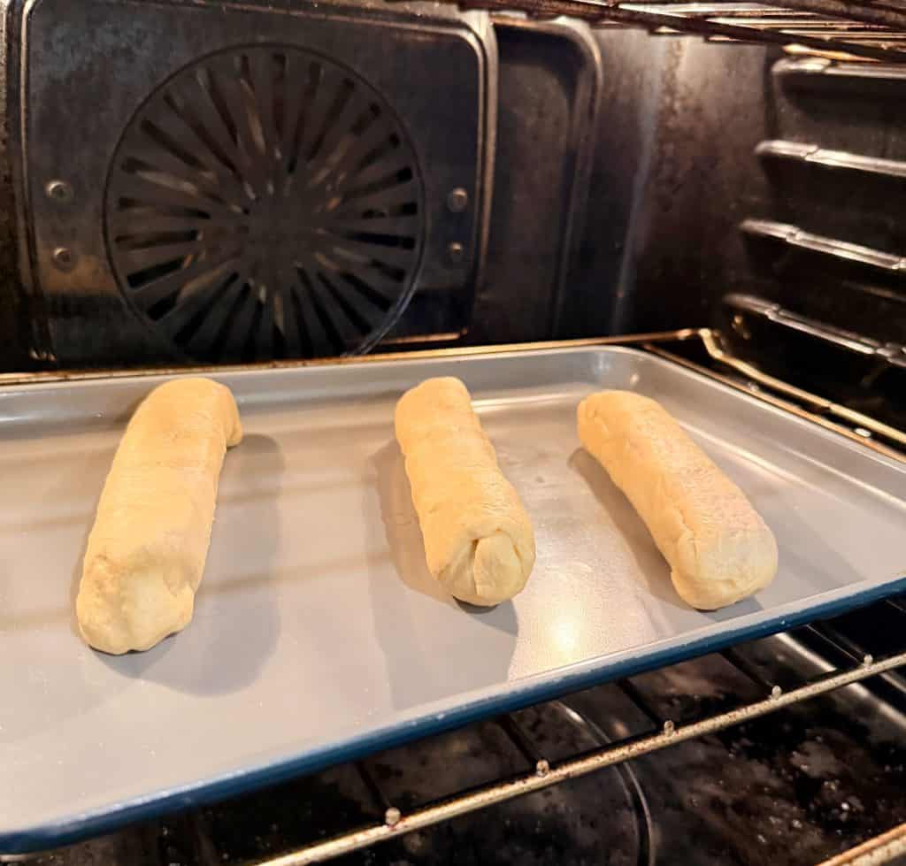 Three unbaked dough logs are placed on a baking sheet inside an oven, ready to be baked.