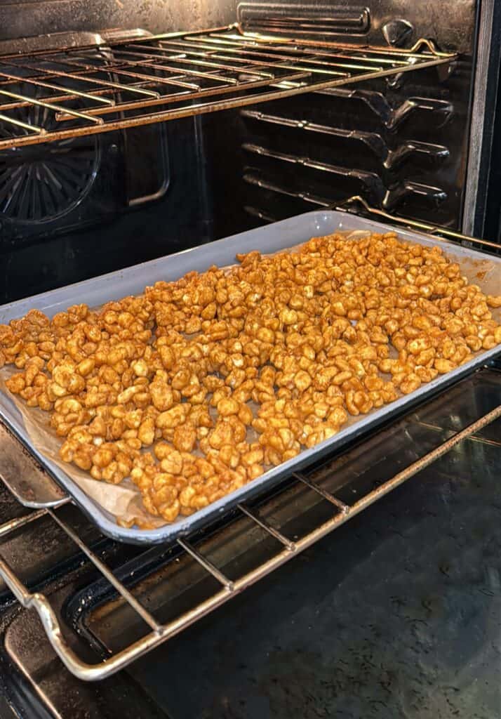 A baking sheet lined with golden caramel-coated puffed rice cereal is placed on the middle rack of an oven for baking.