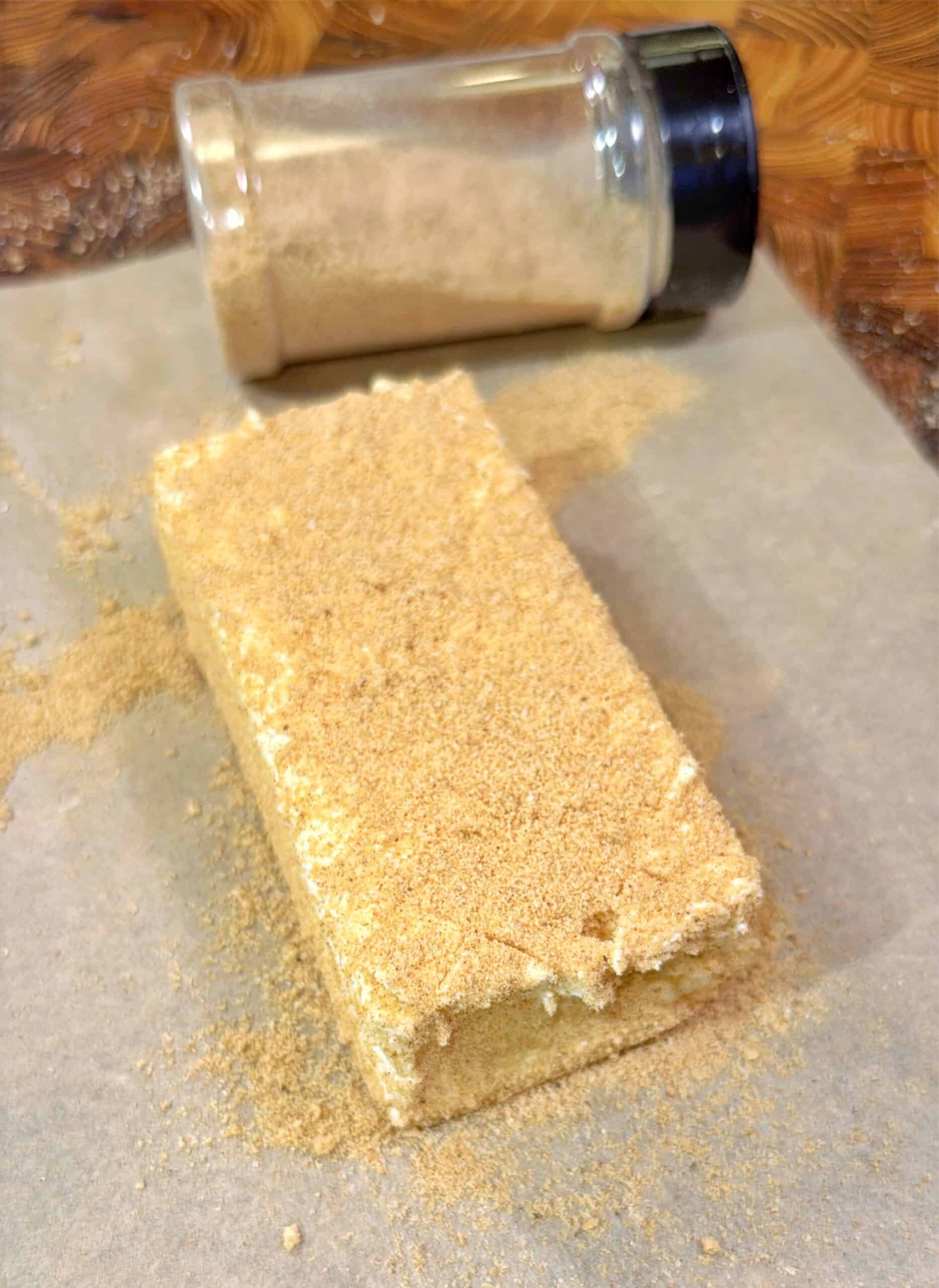 A rectangular block coated in brown sugar sits on parchment paper, with a clear spice jar filled with brown sugar lying on its side in the background.
