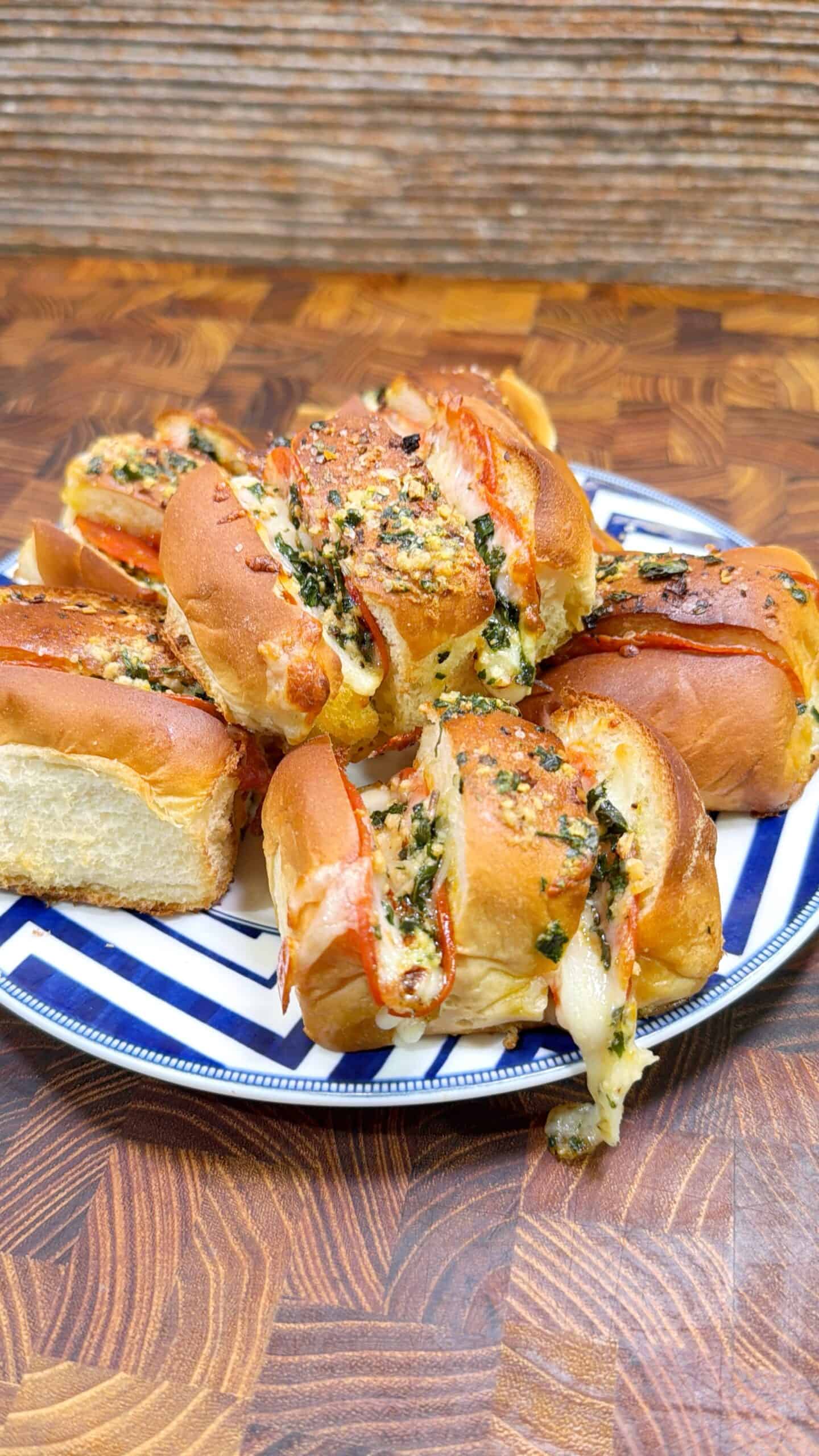 A plate with several cheese-stuffed bread rolls topped with herbs, melted cheese, and a drizzle of sauce, placed on a wooden surface.