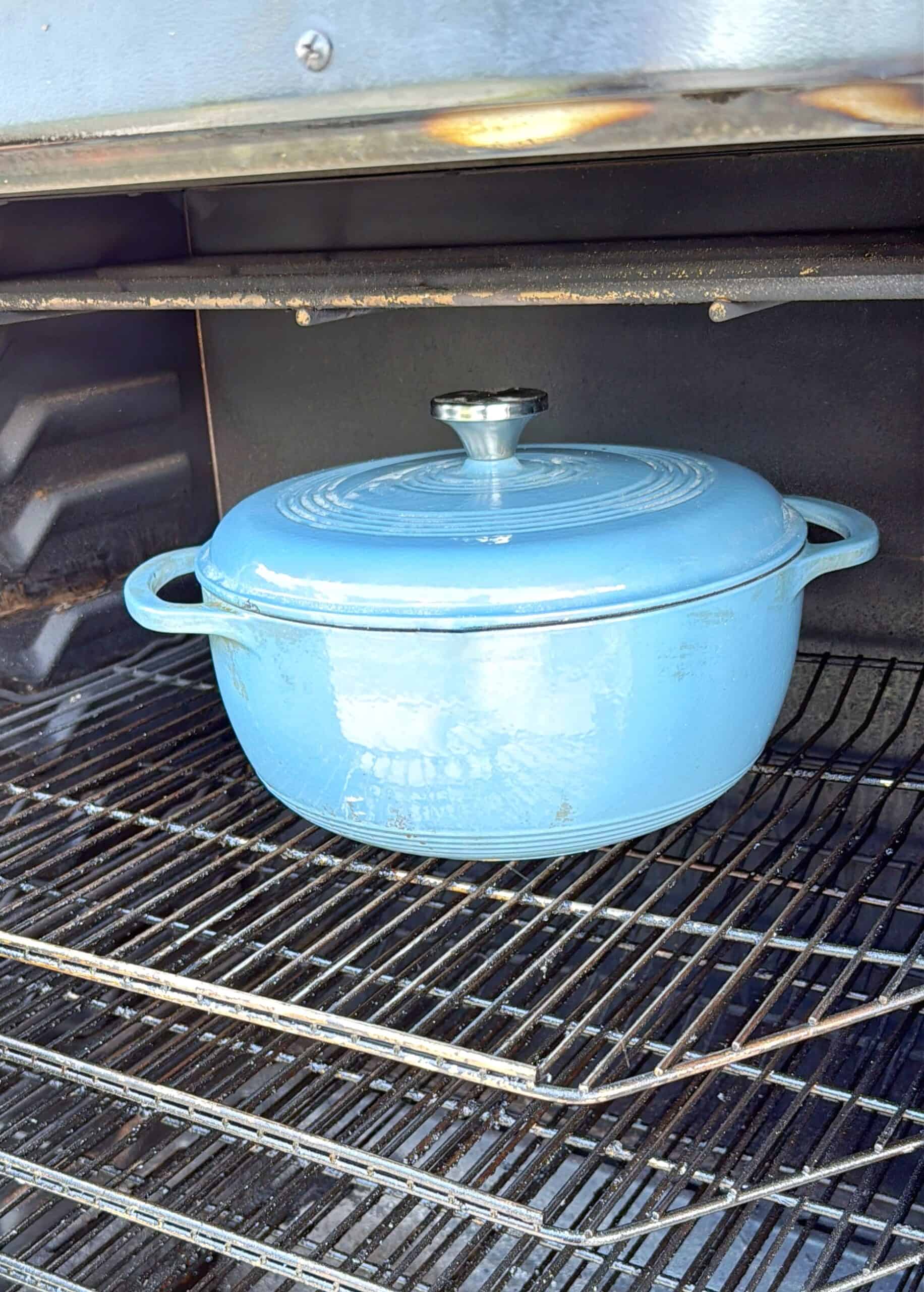 A blue enameled Dutch oven with a lid sits on the middle rack inside an oven, with empty racks above and below it.