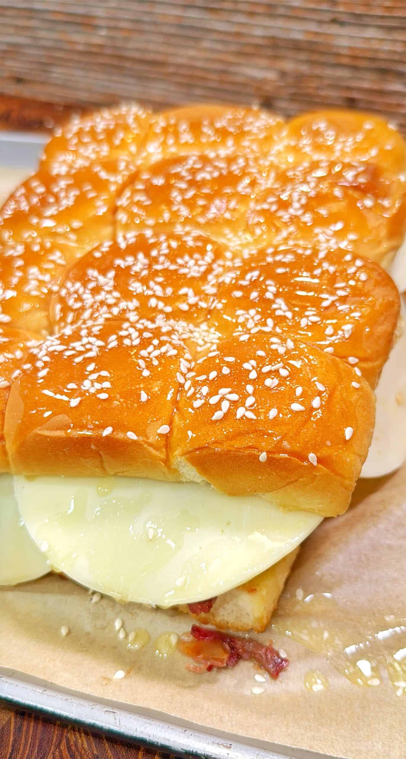 A close-up of a sandwich made with soft, golden, sesame seed-topped buns and thick slices of white cheese, resting on parchment paper.