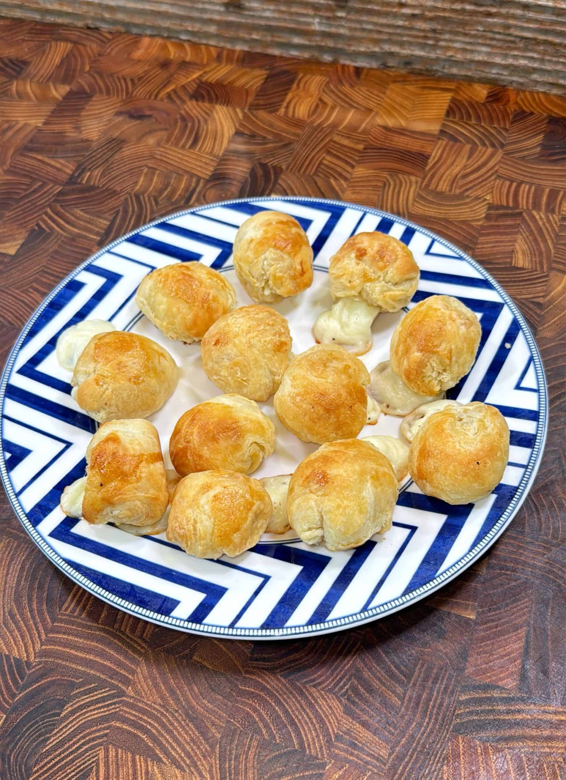A plate of golden-brown, bite-sized pastry puffs is arranged on a white and blue geometric-patterned plate set on a wooden surface.