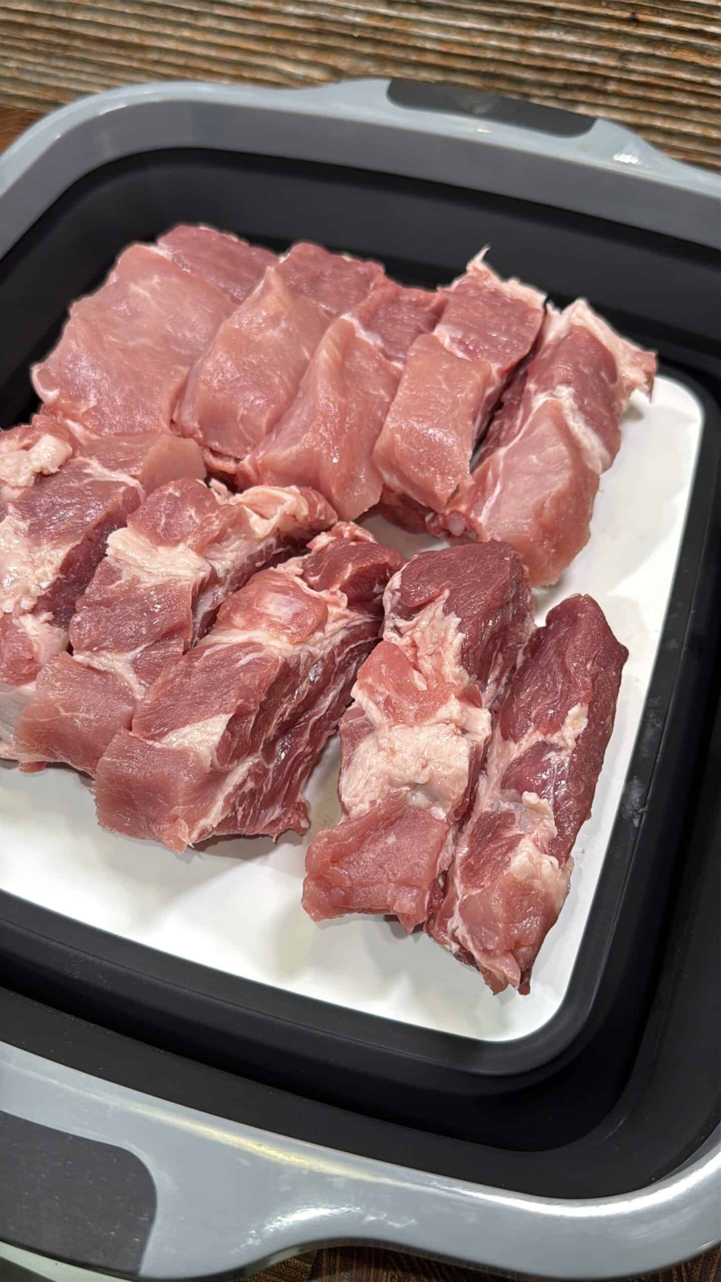 Raw pork ribs cut into strips and arranged neatly on a white tray inside a black container, ready for cooking or seasoning.