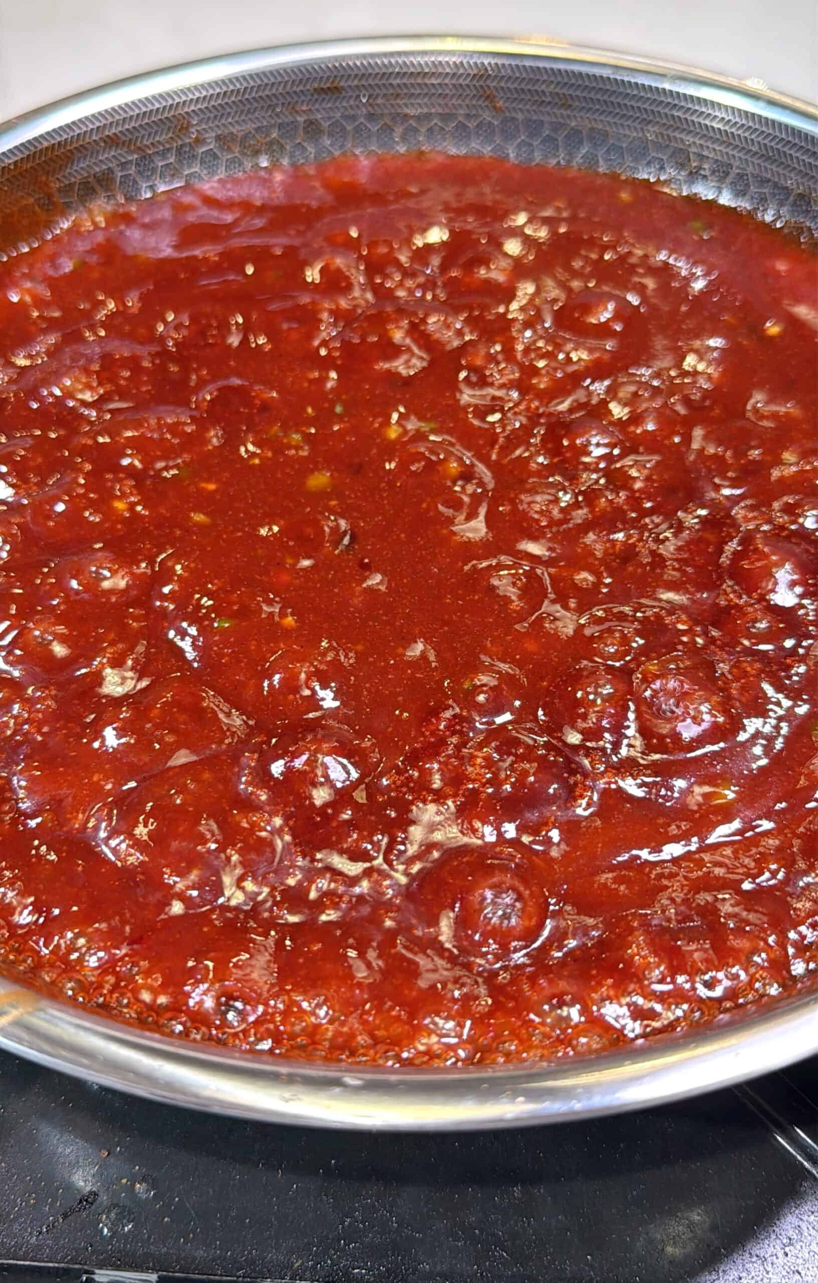 A close-up of a pot filled with bubbling, rich red tomato sauce simmering on a stovetop.