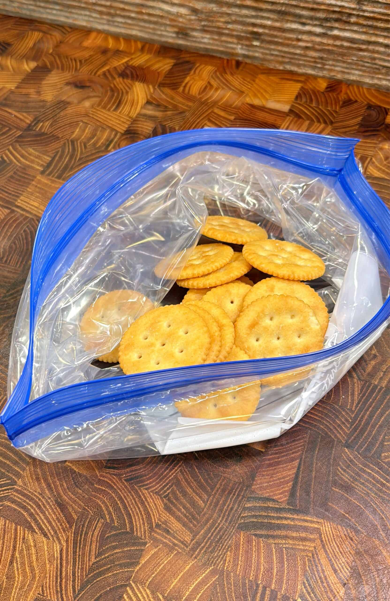 A clear resealable plastic bag partially filled with round, golden crackers sits on a patterned wooden surface.