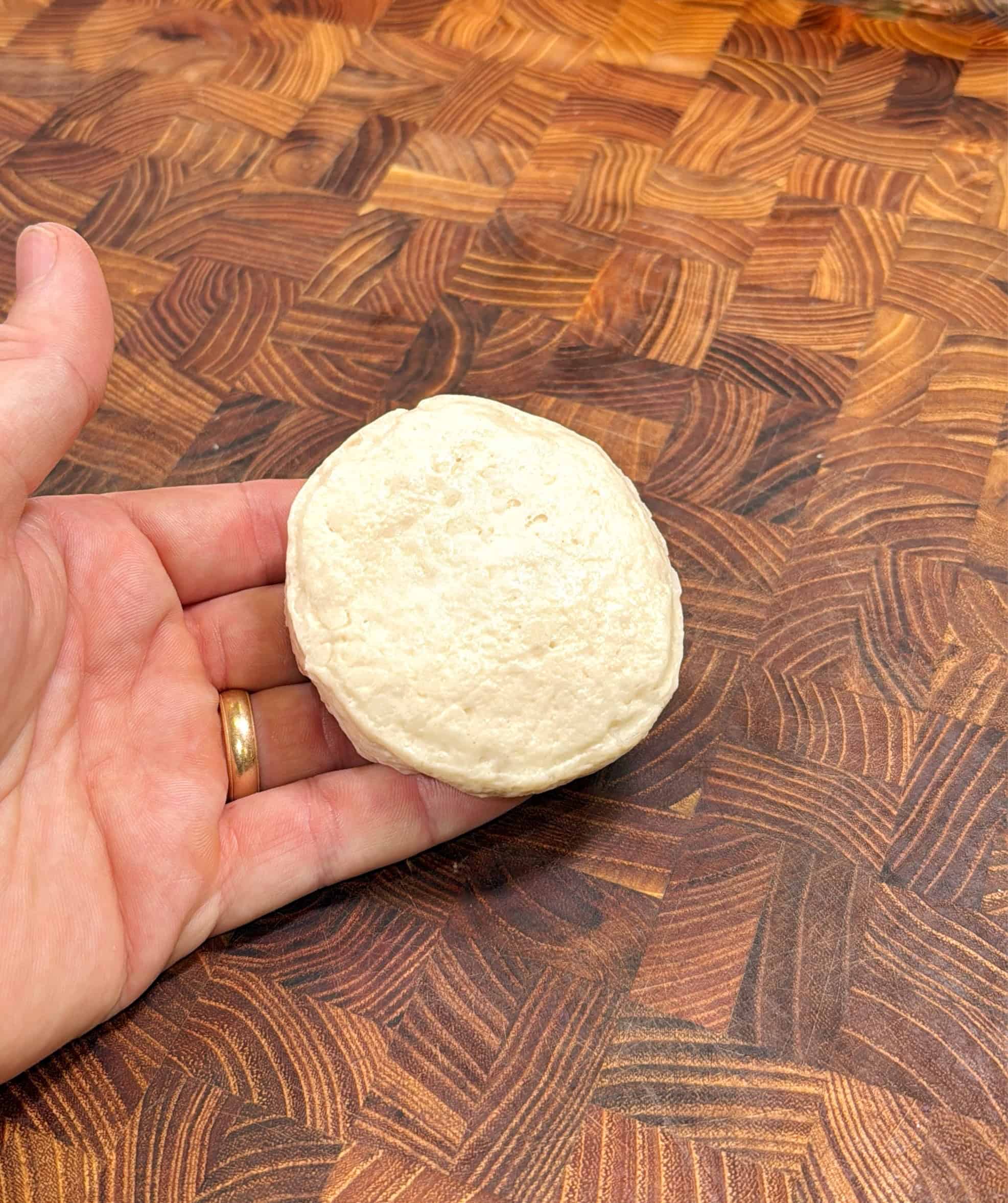 A hand holding a round piece of uncooked dough over a wooden, patterned countertop.