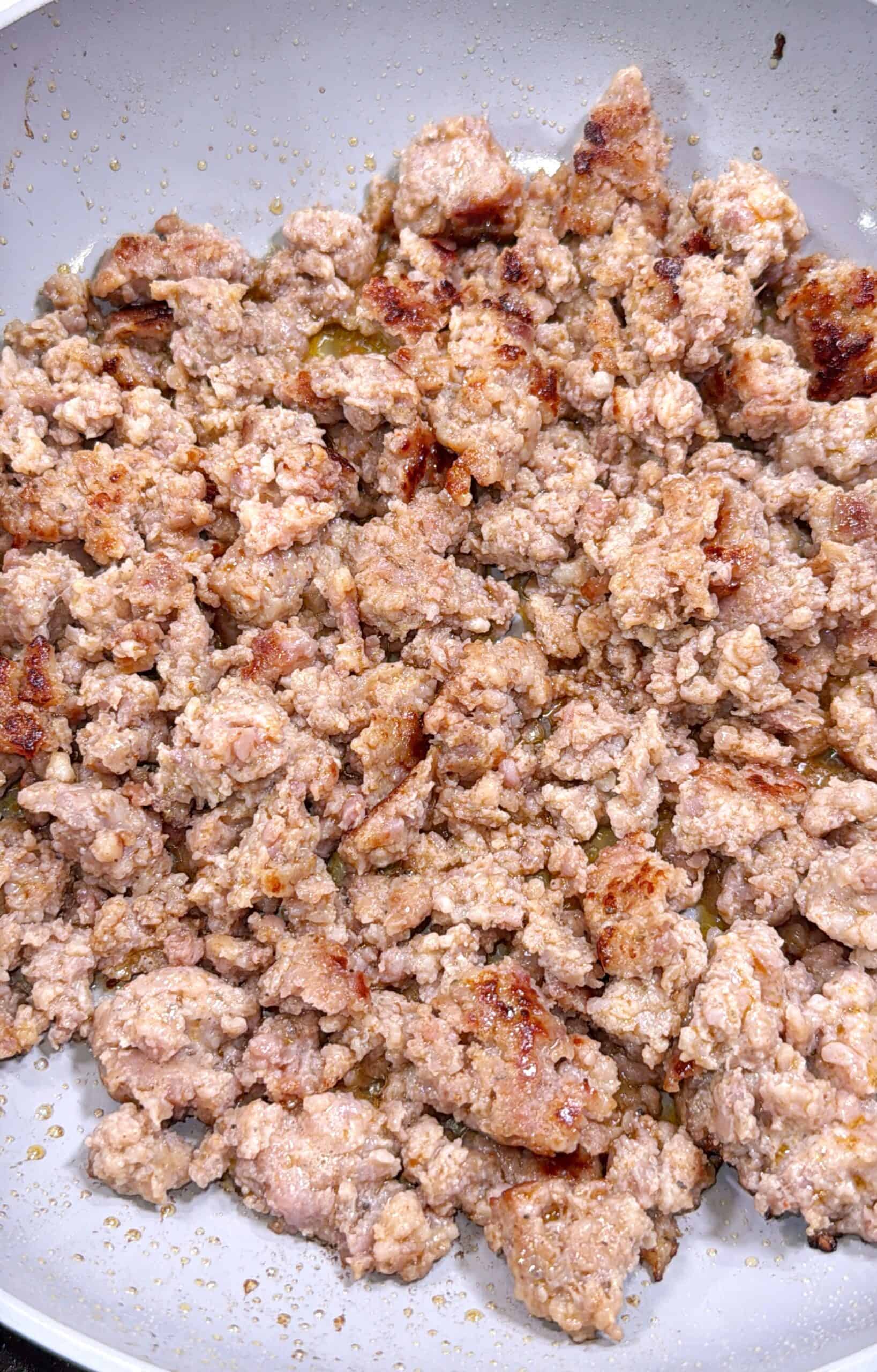 Cooked ground sausage browning in a pan, with some pieces showing a golden-brown sear and a slightly crumbly texture.
