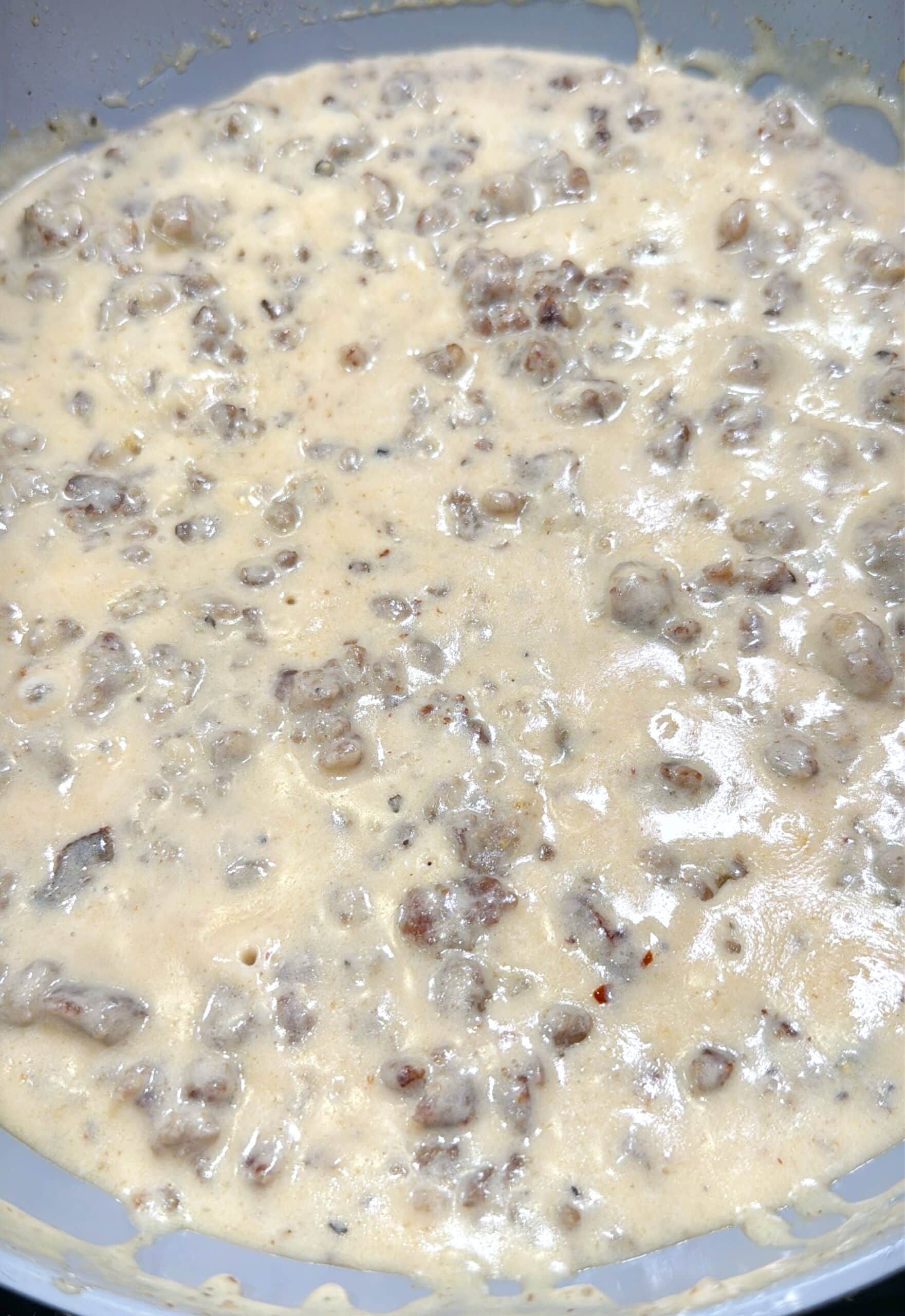 A close-up of creamy sausage gravy with chunks of ground sausage in a thick, beige sauce, commonly served as a breakfast dish.