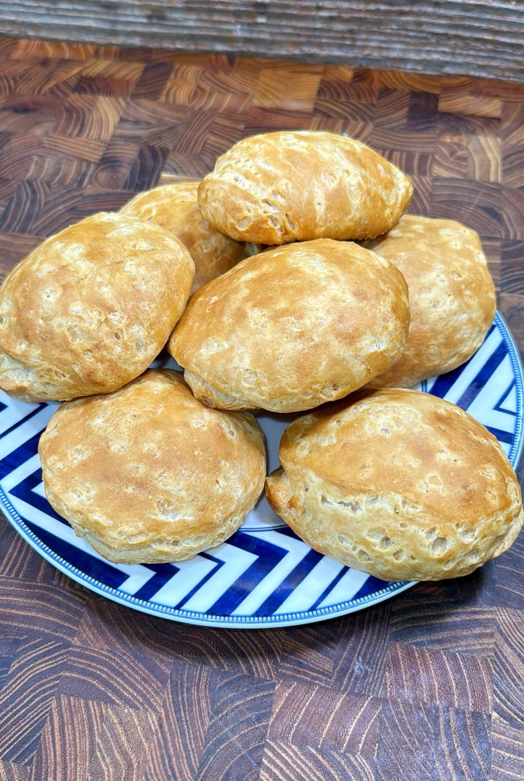 A plate with seven golden-brown breakfast bombs is placed on a wooden surface. The plate has a blue and white geometric pattern around the rim.