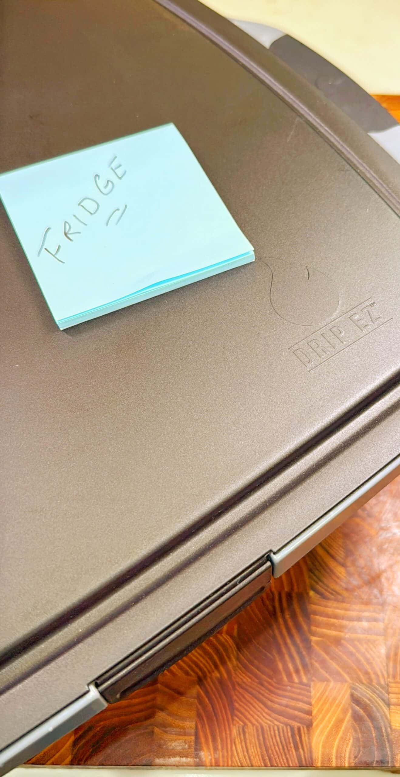 A blue sticky note labeled FRIDGE sits on top of a closed brown appliance with the word FRIDGE faintly embossed on its surface.