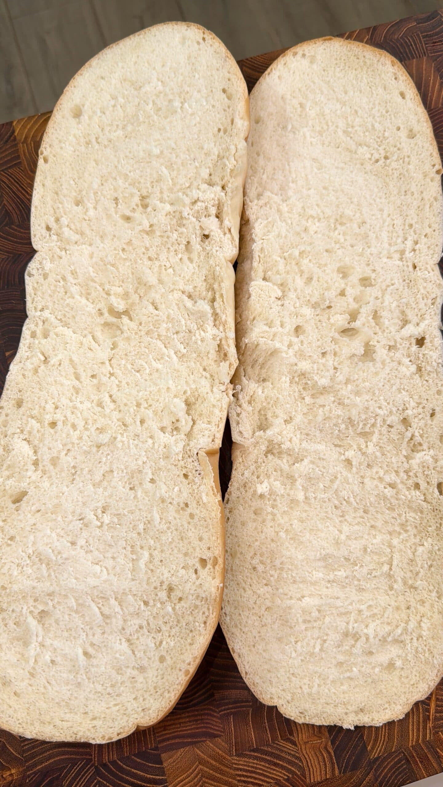 Two halves of a plain, sliced sandwich roll placed side by side on a wooden surface, showing the soft, airy interior of the bread.