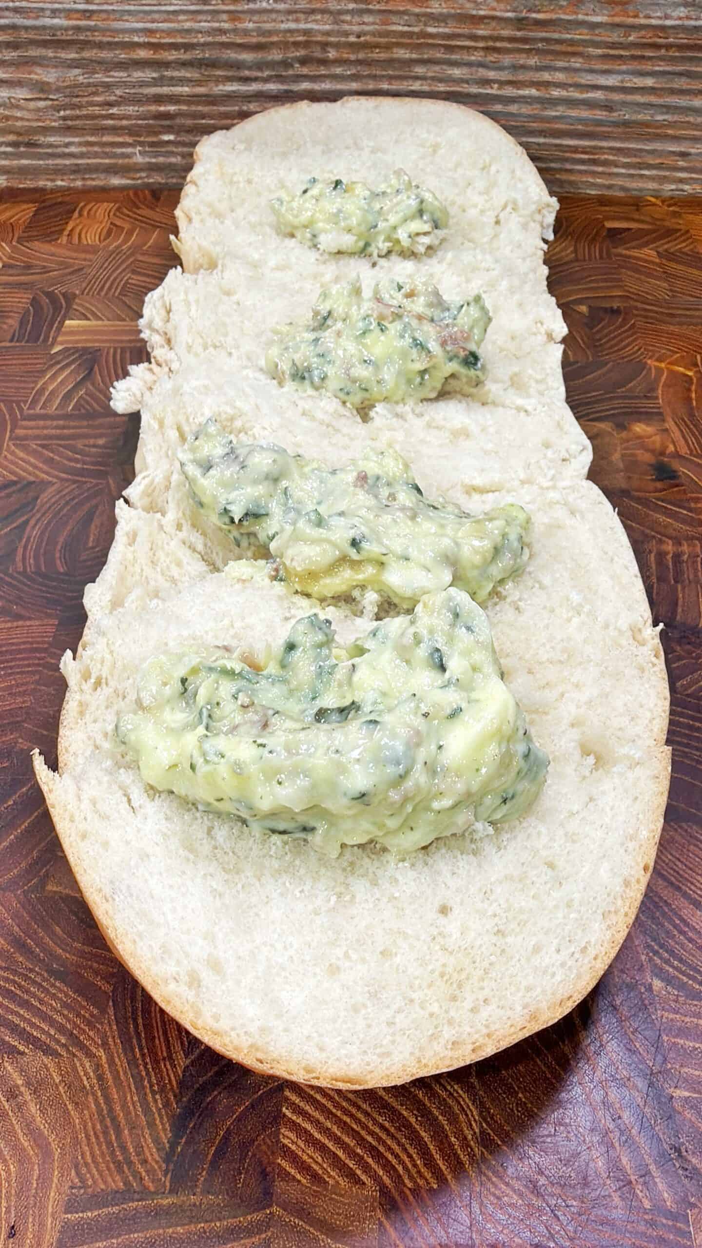 A split loaf of white bread on a wooden surface, with four dollops of a creamy spinach and cheese mixture spread evenly along the inside.