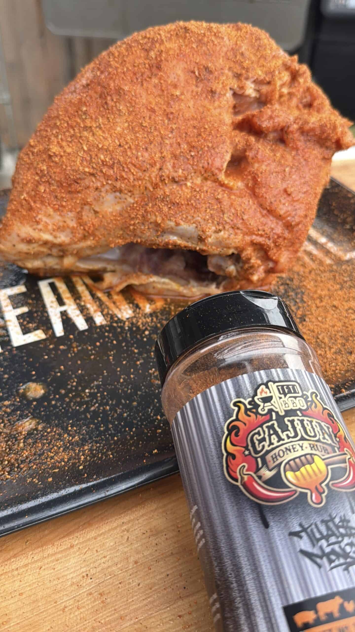 A large turkey breast coated in a reddish-brown Cajun dry rub sits on a black cutting board, with a bottle of Cajun Honey Rub seasoning displayed in the foreground.