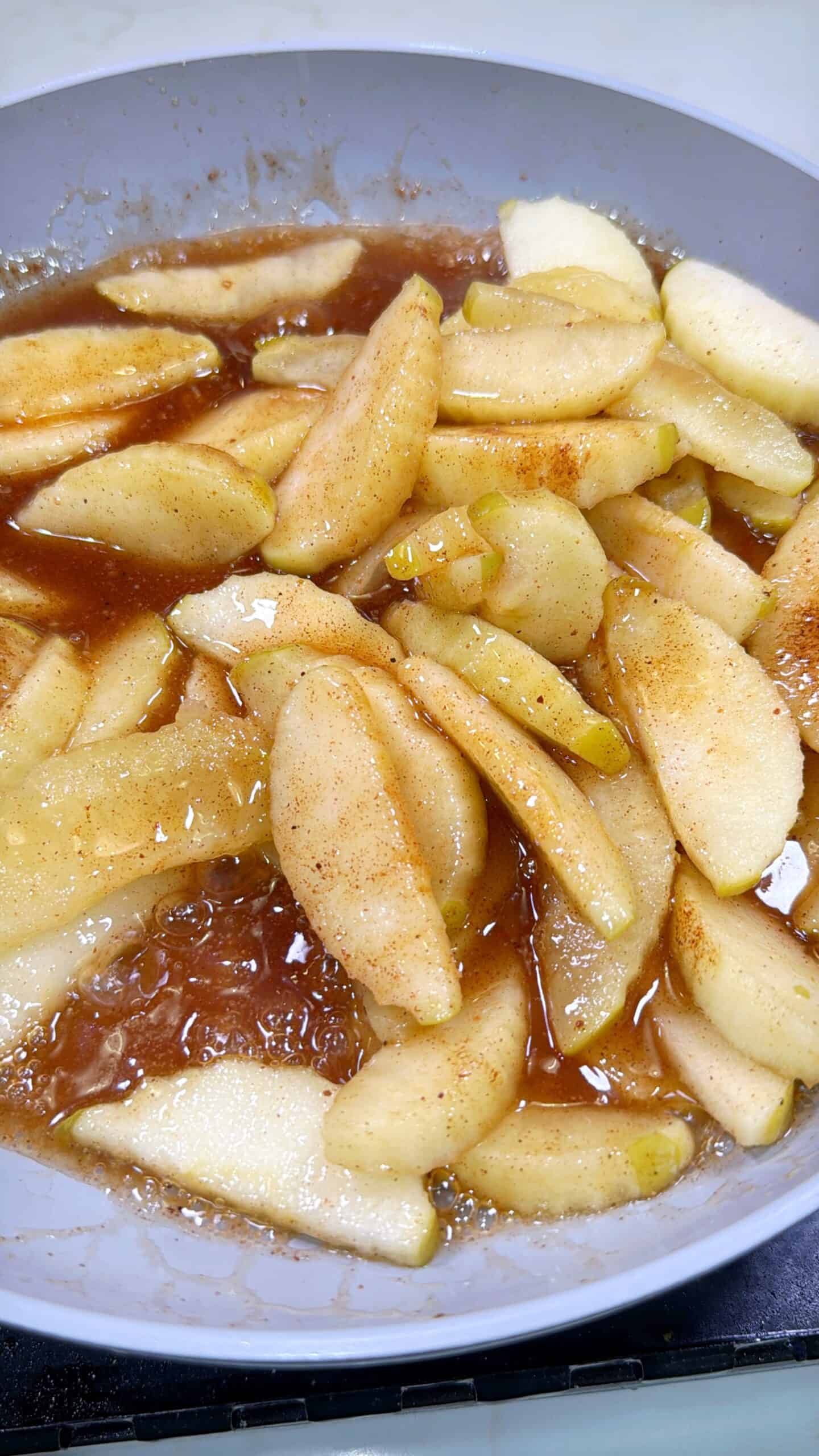Sliced apples cooking in a pan with cinnamon and sugar, creating a syrupy mixture.