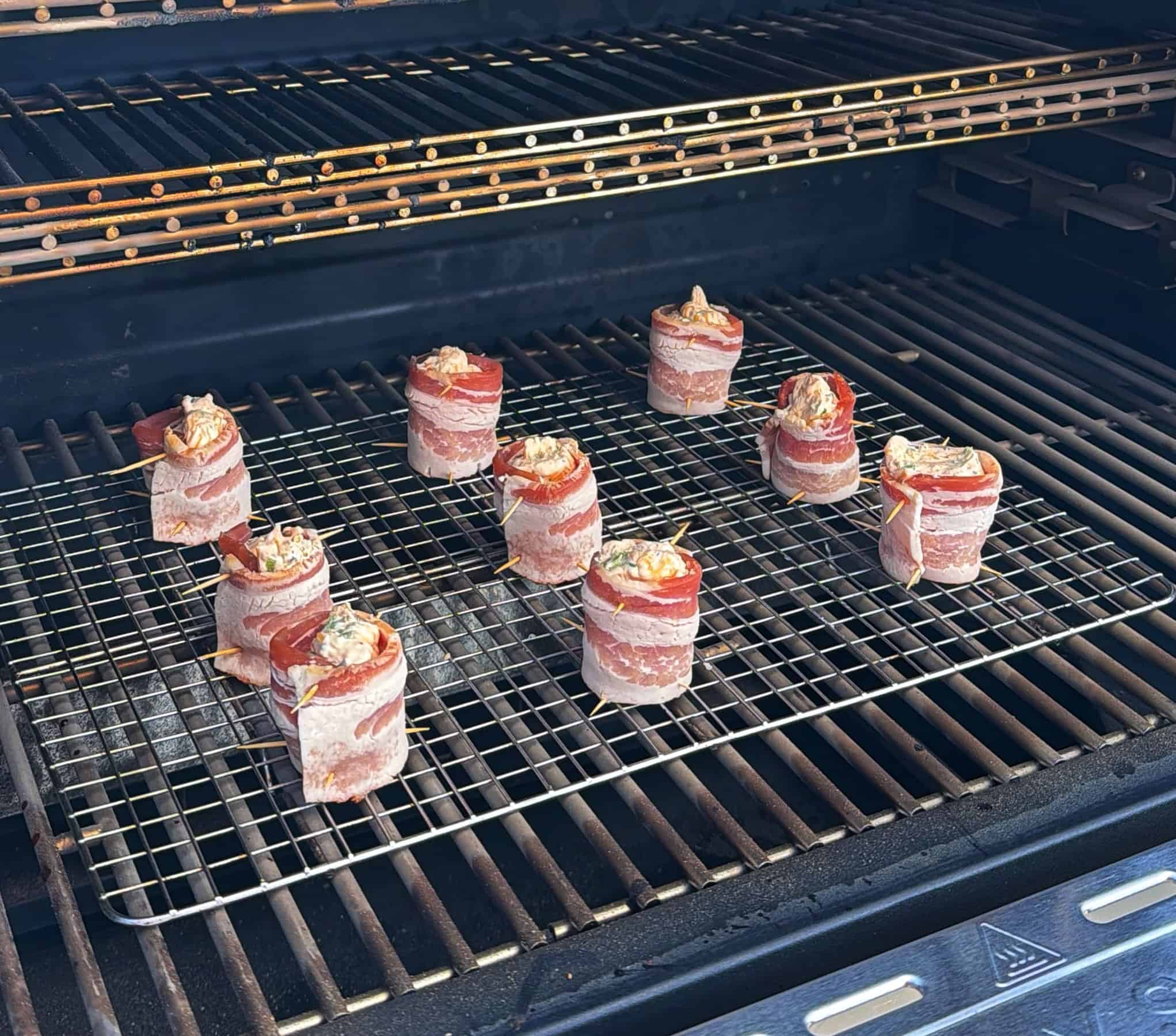 Several bacon-wrapped meat bundles, possibly stuffed, are arranged on a wire rack inside a barbecue grill, ready to be cooked.