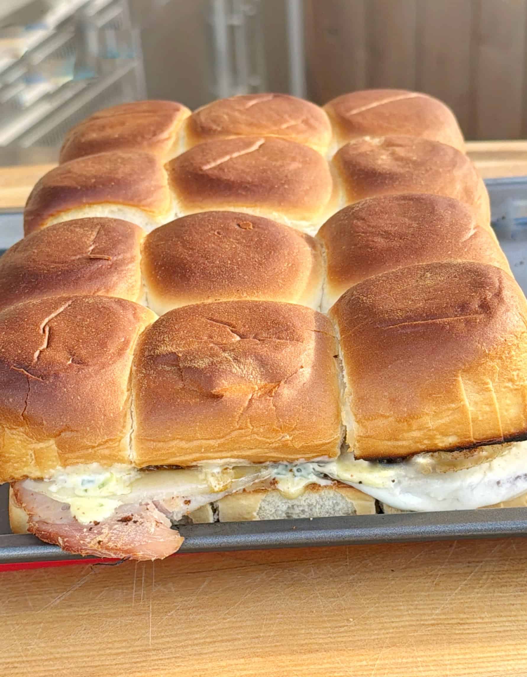 A tray of baked slider sandwiches with golden-brown tops; some sandwiches have bacon, egg, and cheese visible between the buns.