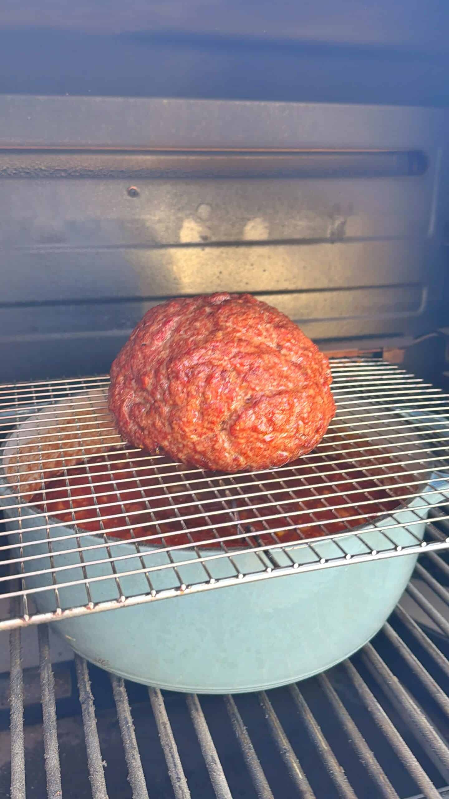 Smoked over the top chili where raw ground meat sits on a wire rack inside an oven or smoker, with a blue dish underneath to catch drippings.