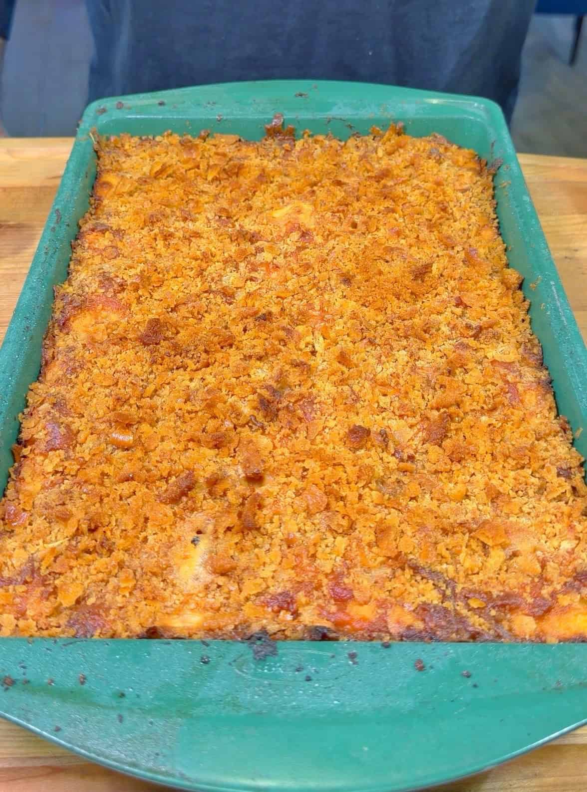 A green baking dish filled with a casserole topped with a golden-brown, crispy breadcrumb crust sits on a wooden surface.