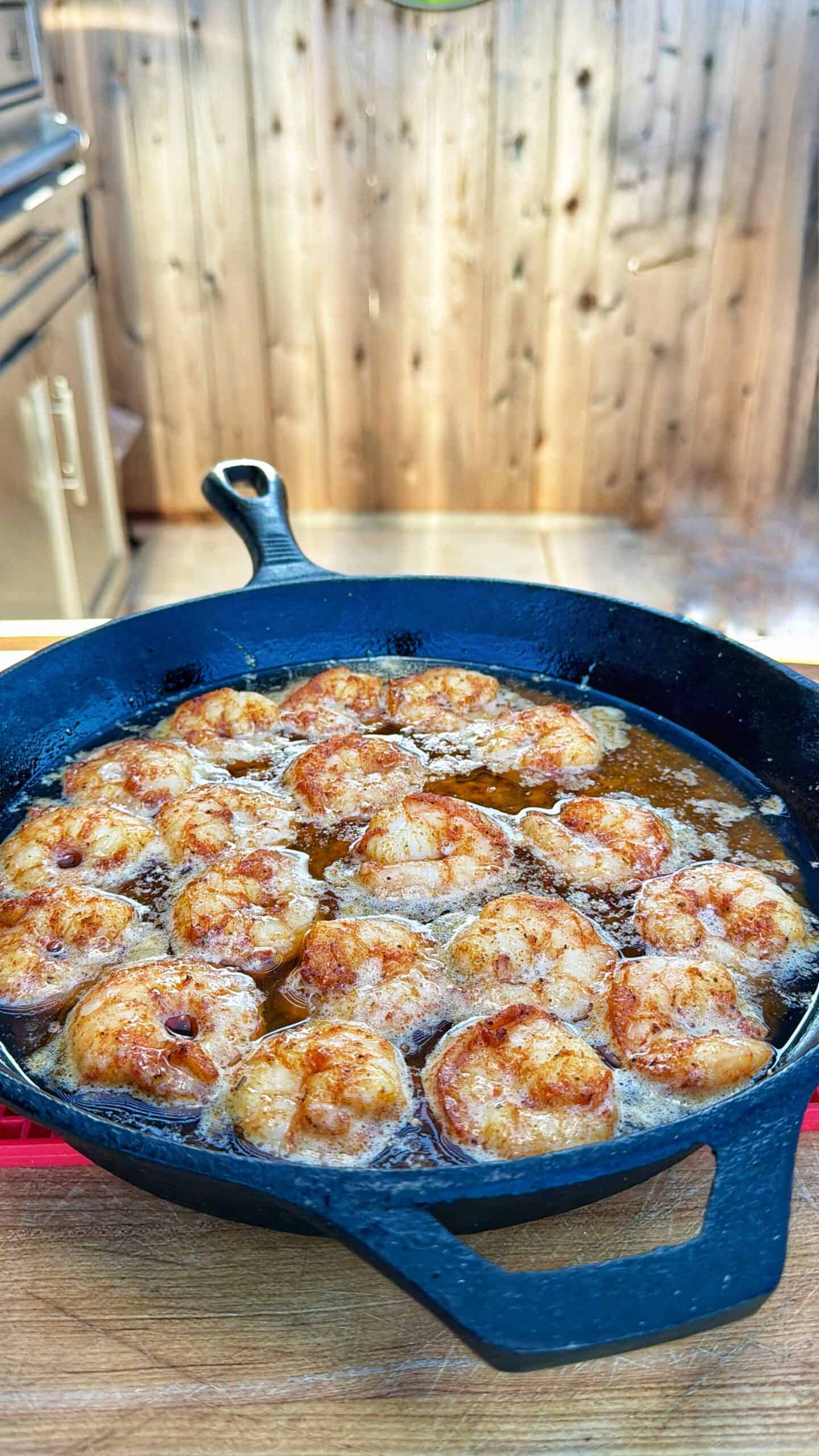 Cajun Honey Shrimp sizzling in a cast iron skillet filled with bubbling oil, cooking outdoors on a wooden surface with a blurred wooden fence in the background.