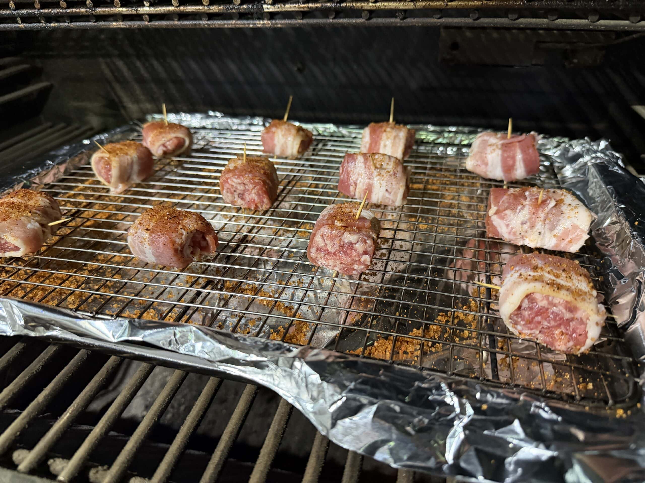 Bacon Wrapped Brat Bites are secured with toothpicks and arranged on a wire rack over a foil-lined baking sheet in the grill or oven, then sprinkled with seasoning for the perfect appetizer.