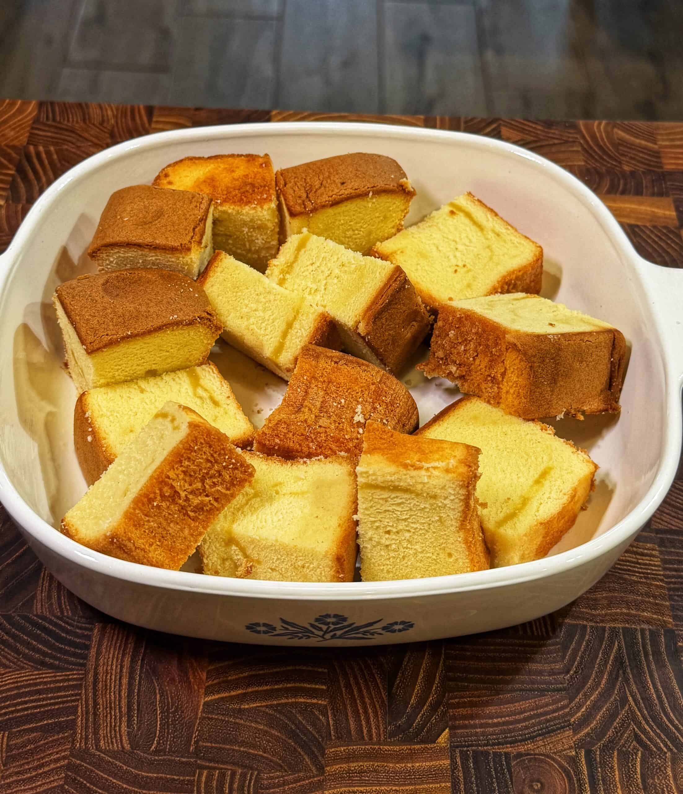 A white dish with a blue floral pattern holds several thick, square slices of golden brown pound cake, arranged neatly on a wooden surface.