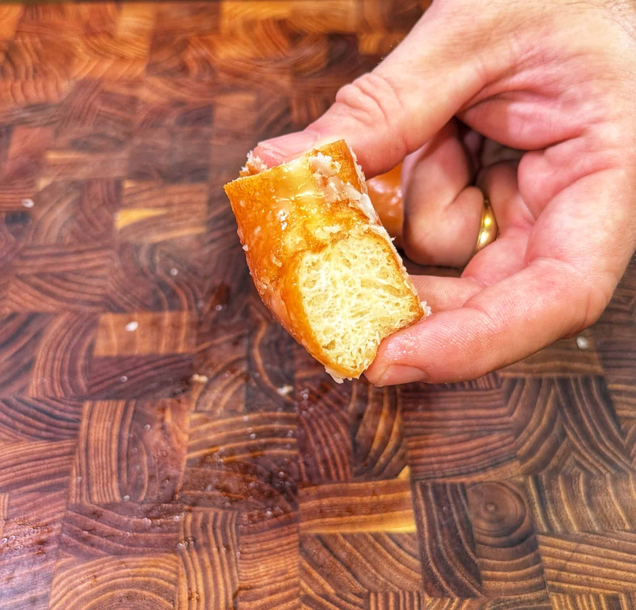 A hand holding a half-eaten glazed donut with a fluffy, airy interior, over a patterned wooden surface.
