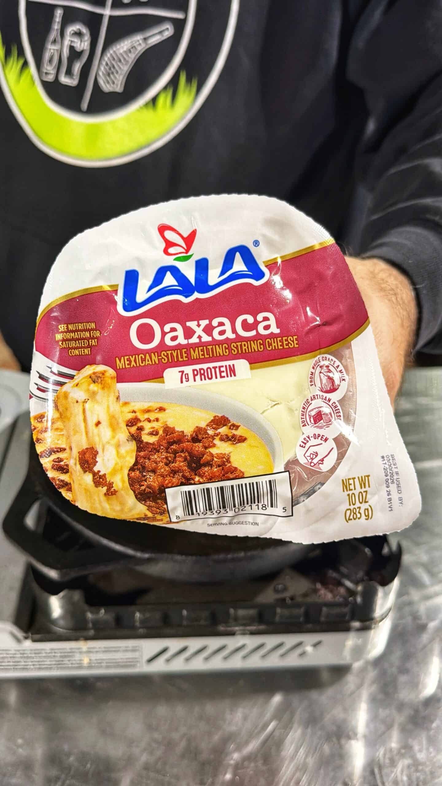 A person holds a package of LALA Oaxaca Mexican-style melting string cheese with 7g protein per serving. The label shows melted cheese and food, and the package weighs 10 oz (283g).