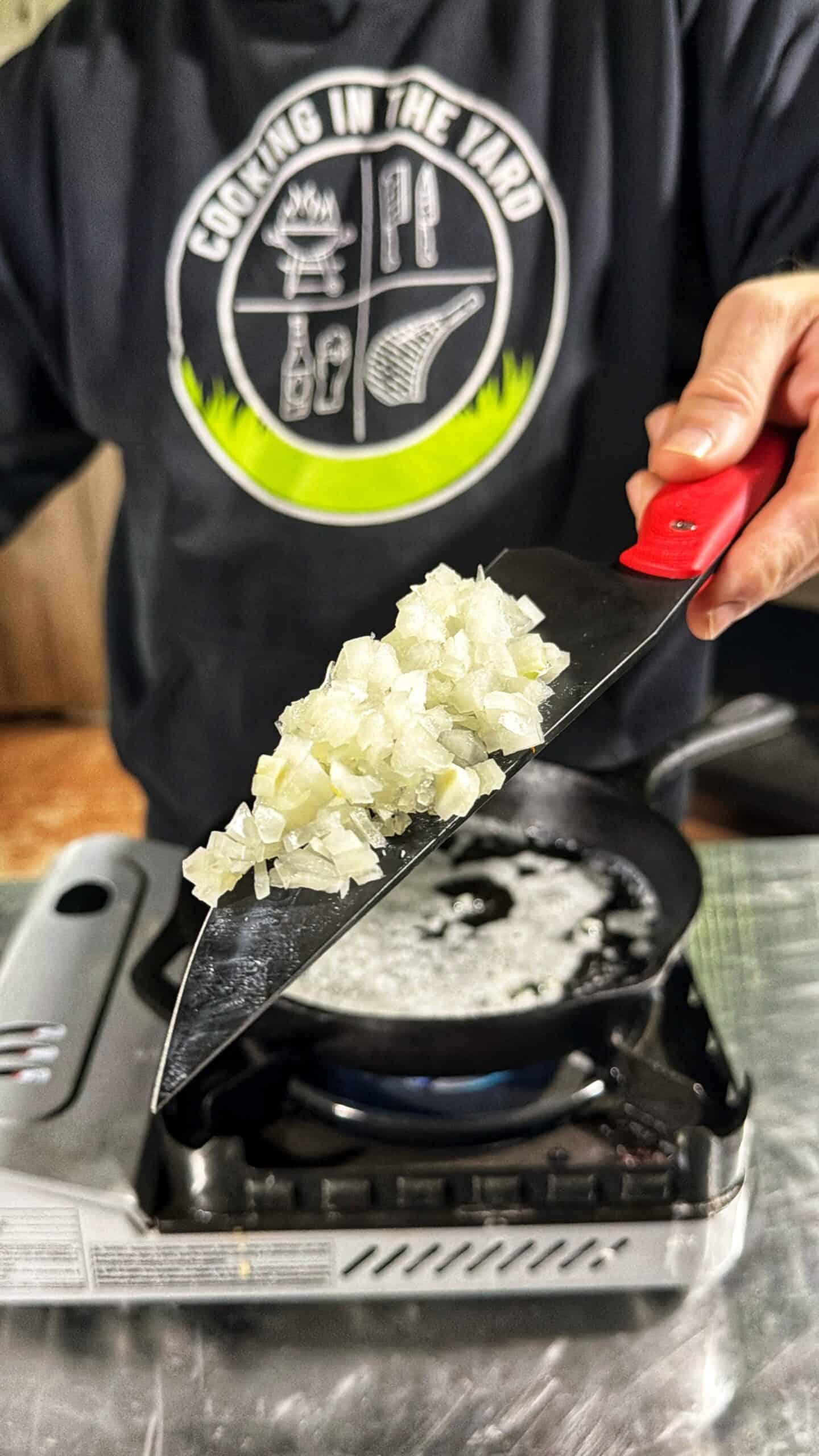 A person holding a knife with onions on it.