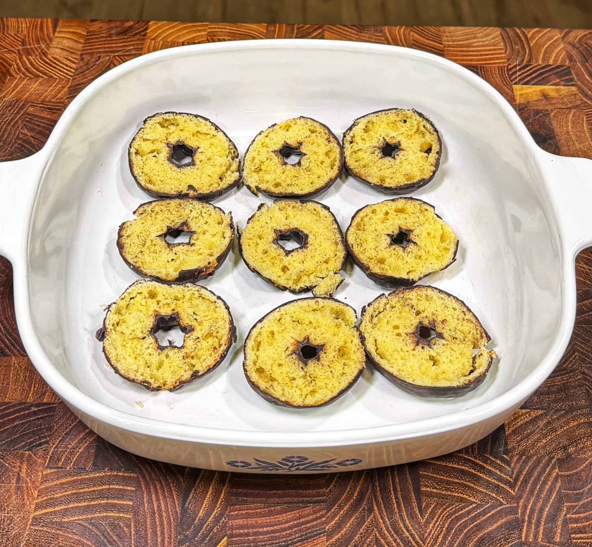 A white ceramic baking dish holds nine round slices of cake, each with a star-shaped hole in the center. The cake slices appear to be coated in chocolate on the edges and arranged in a grid pattern.